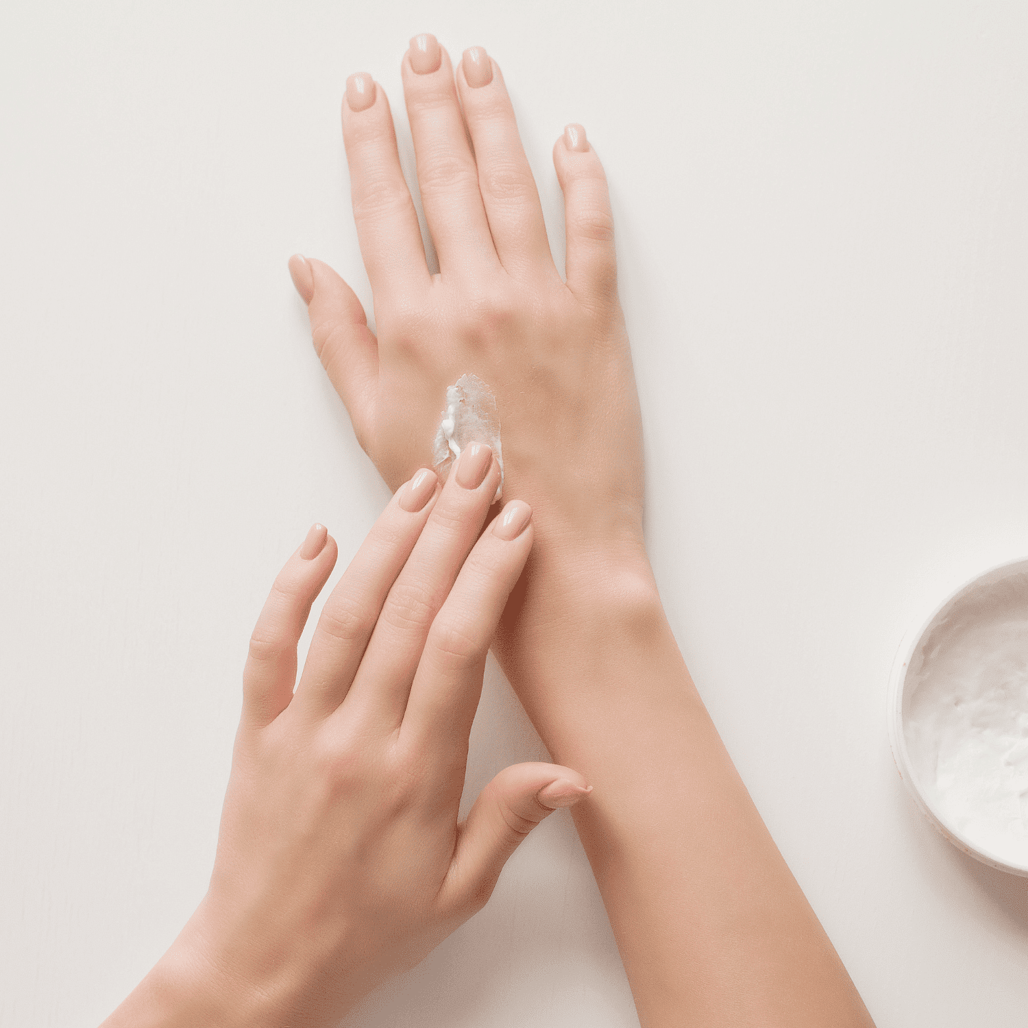 Applying moisturizer to hands on a white background.