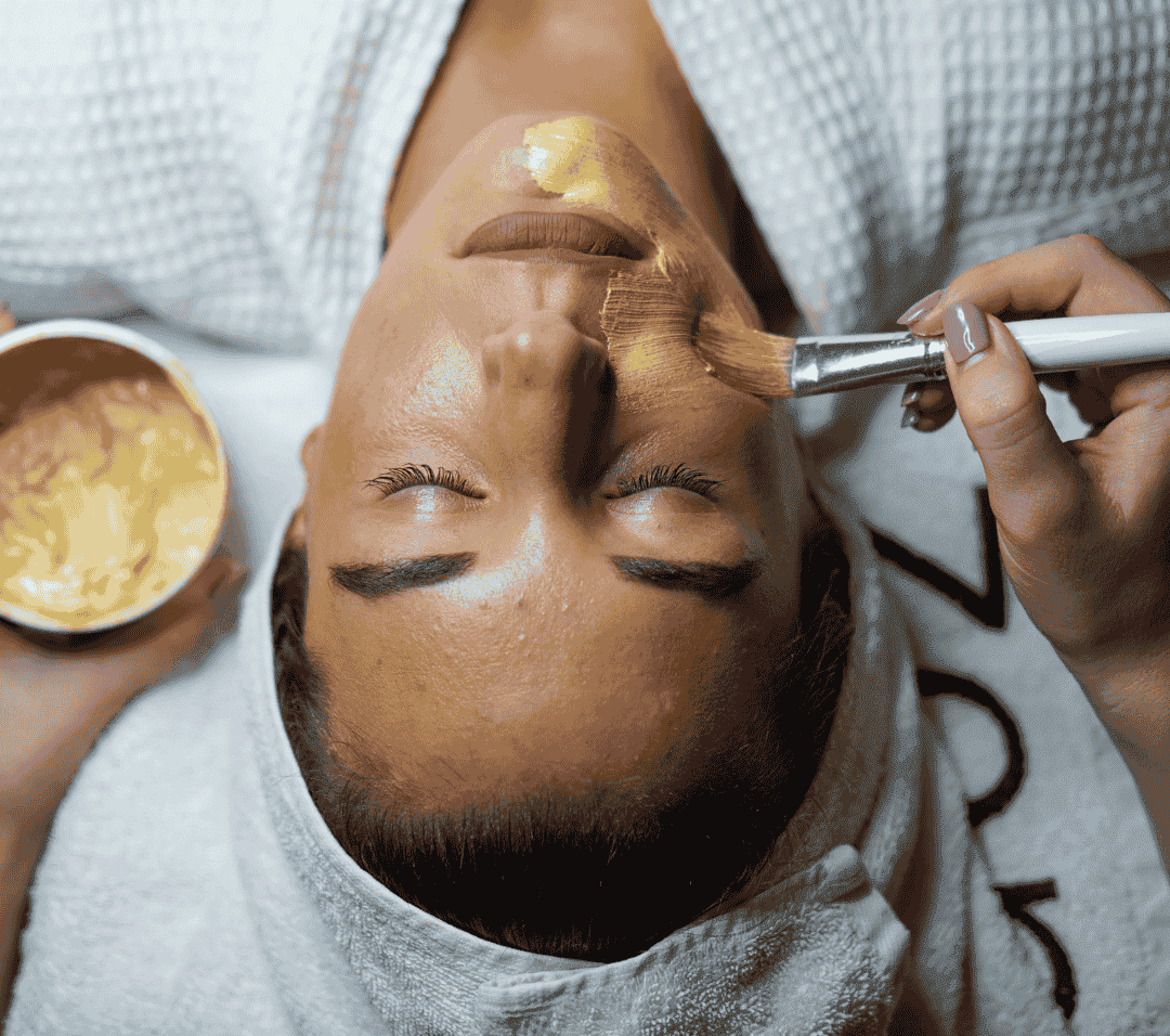Facial treatment with golden mask applied by brush in spa setting.